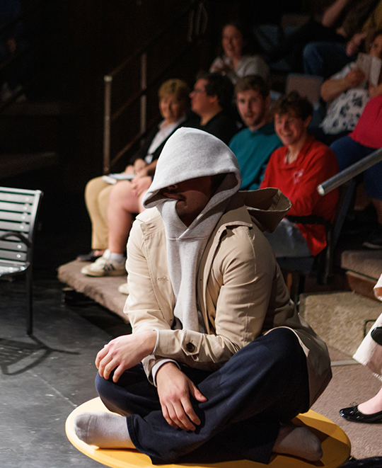 Dates show with a person seated crossed legged on a coffee table with his hoodie pulled all the way over his face