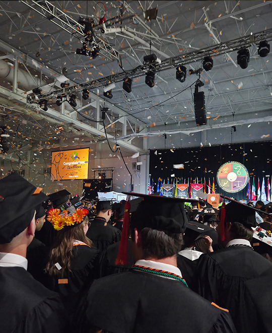 graduation ceremony, with confetti falling over graduates wearing black gowns and caps