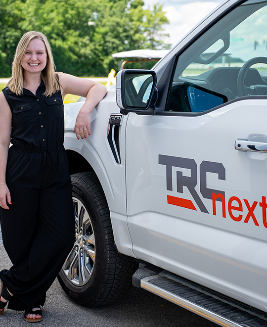 Taylor Weideling smiling and standing next to a white TRC vehicle.
