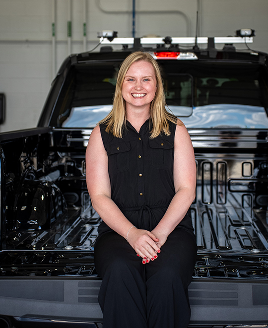 Taylor Weideling smiling and seated on the back of a black truck bed.