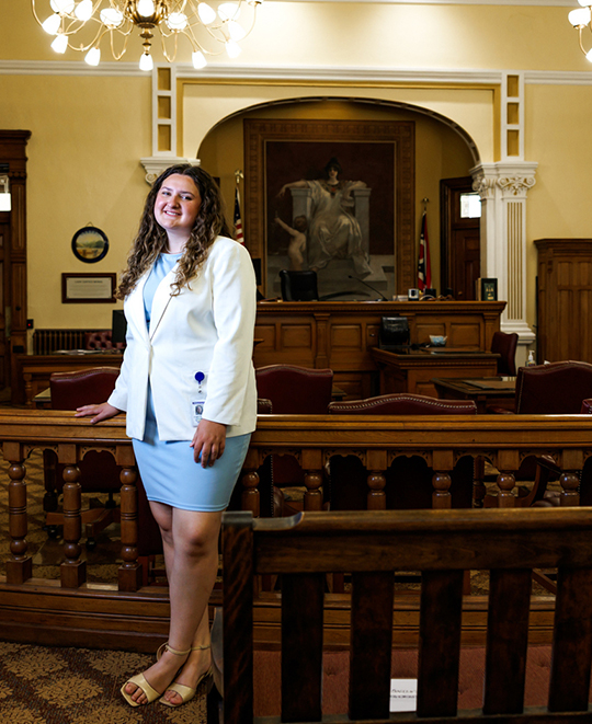 Evelynn Schneider wearing a white jacket and blue skirt, standing inside the Hancock County Court of Common Pleas courtroom.