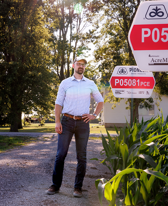 Alumnus Dr. Eric Schultz standing on a paved path next to lush trees and a red and white agricultural sign.