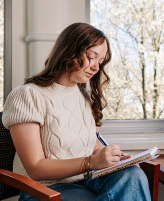 Evie Megery seated and looking down while writing in a notebook