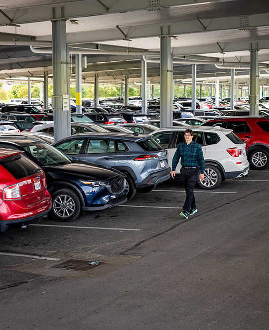 Chase McCluskey walking through a spacious modern facility with rows of vehicles visible indoors in the background.