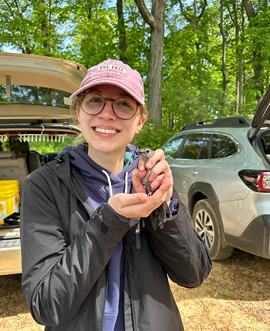 Cora Neville smiling while carefully holding a small songbird during field research.