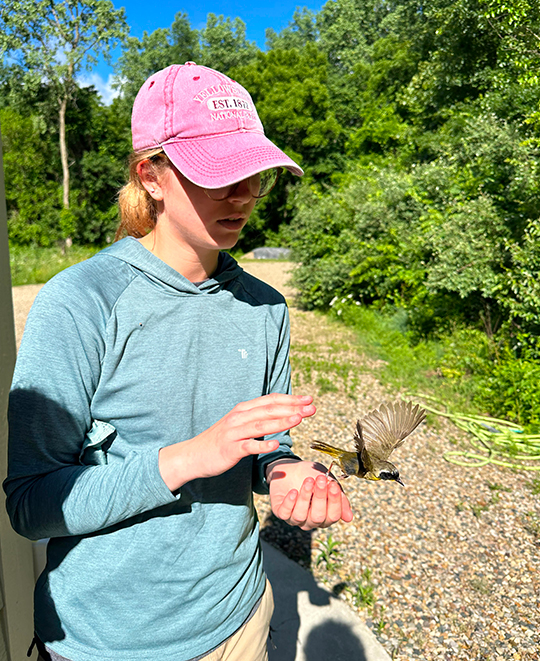 Cora Neville standing in a field wearing a pink hat during wildlife research.