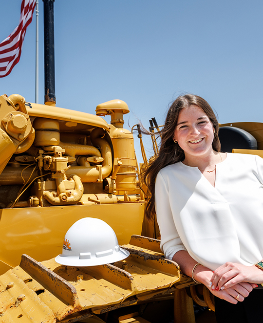 Emersyn Gerken sitting in front of heavy construction equipment on a job site.