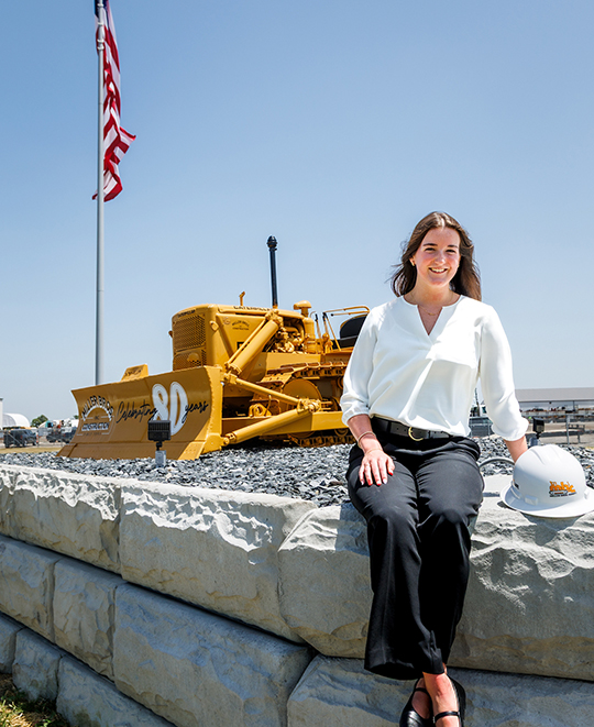 Emersyn Gerken at a Miller Bros. Construction job site with heavy equipment in the background.