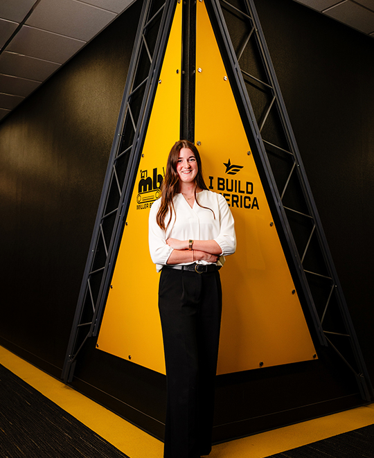 Emersyn Gerken wearing a white blouse and white pants, standing indoors between colorful architectural display panels.