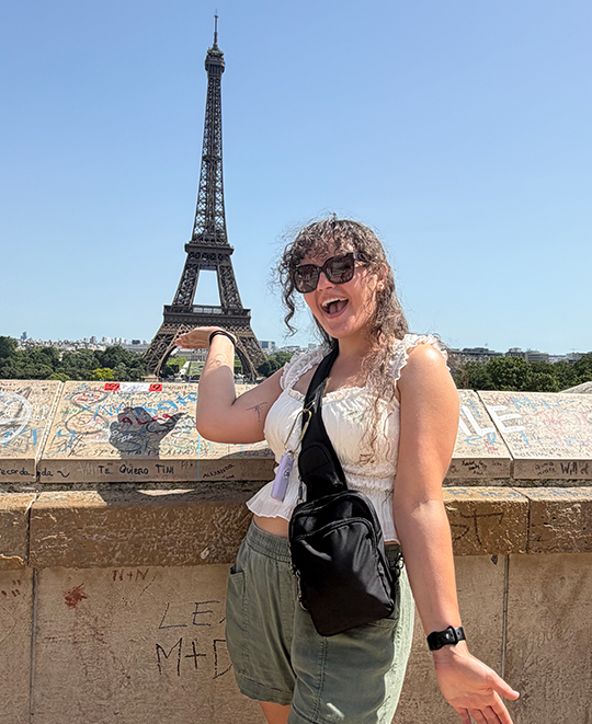 Elizabeth Gruen sitting outdoors in Paris with the Eiffel Tower visible in the background.