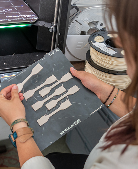 Maddie Whitewolf holding and examining a tray of 3D-printed tensile test specimens.