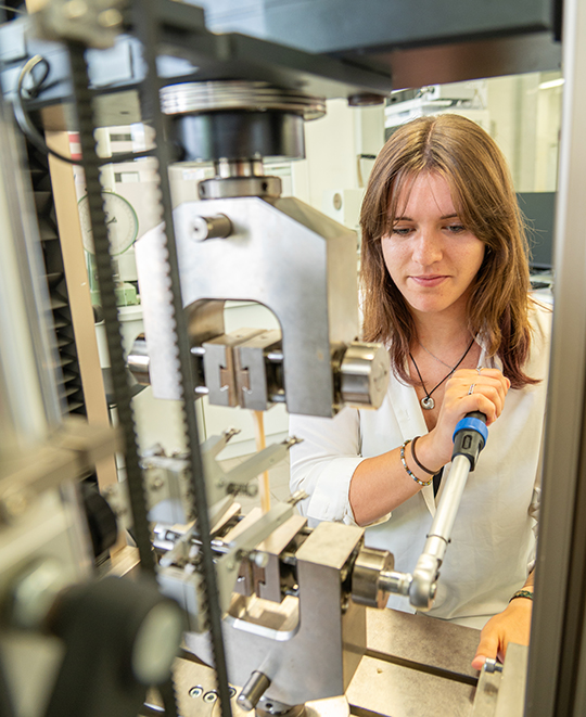 Maddie Whitewolf standing next to complex laboratory machinery and holding a clear container.