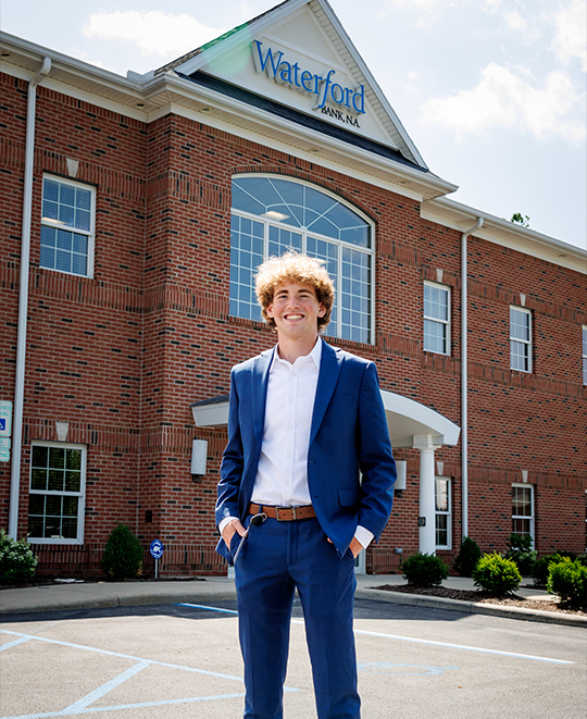 Ohio Northern University student Tyler Wood wearing a blue suit, standing outdoors in front of a brick building for Waterford Bank.