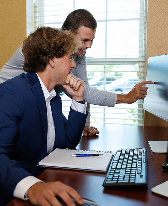 Ohio Northern University student Tyler Wood leaning over a computer monitor to discuss financial data with a colleague in an office.