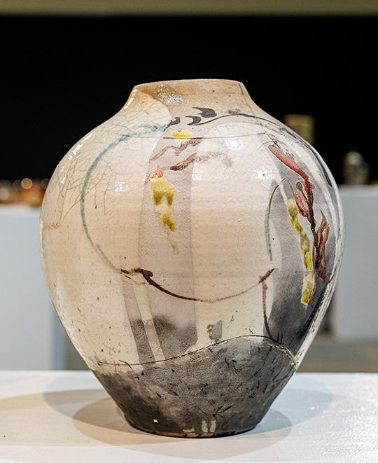 Rounded, pale ceramic vessel with a narrow spout and textured, earth-toned glazed patterns crafted by Bruce Chesser.
