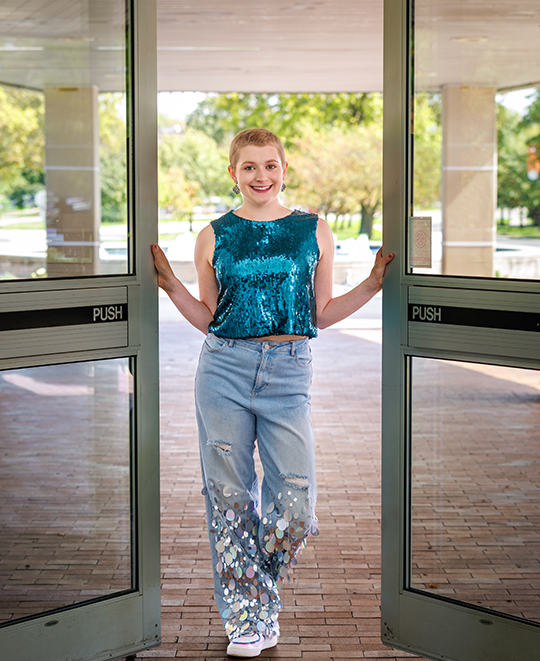 Cassandra Kurek smiling as she walks through glass doors on campus.