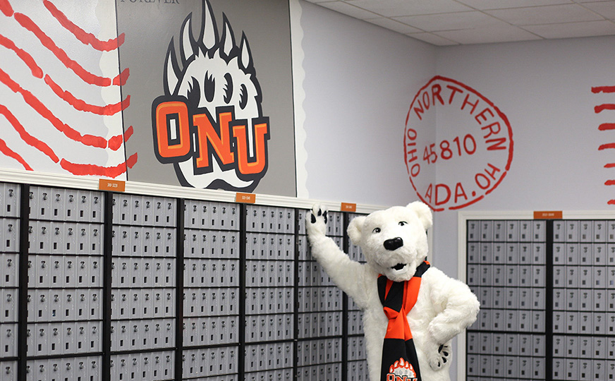 ONU mascot Klondike waving in front of student campus mailboxes.
