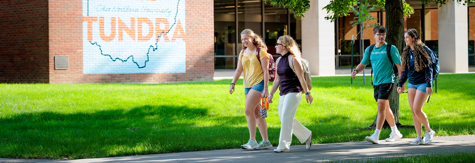 Students walking together on a green campus lawn in front of Ohio Northern University campus buildings.