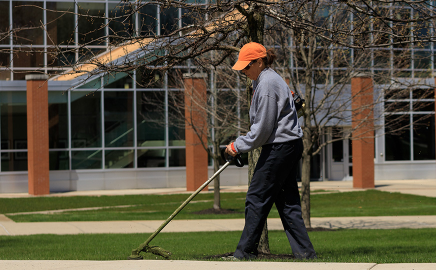 Groundskeeper maintaining the Ohio Northern University campus lawn in front of an academic building.