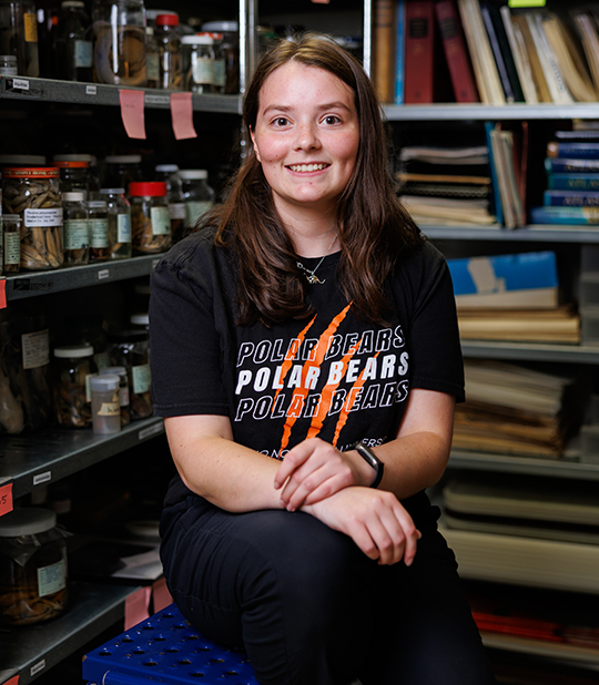 Jacey Wonderly smiling in front of lab shelves filled with specimens and equipment.