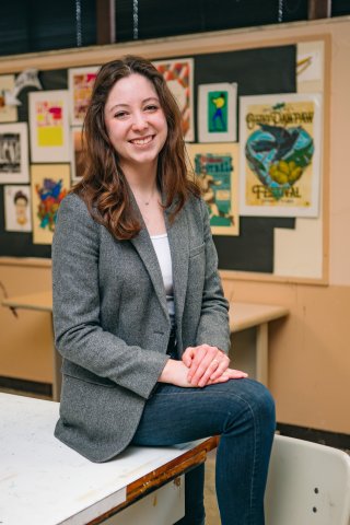 Another photo of Carmen seated on a table with art work behind her