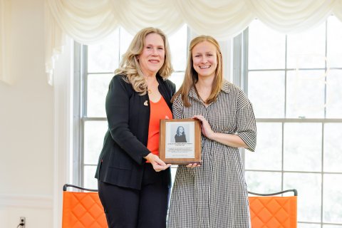 Two people hold a plaque while dressed in professional attire