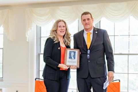 Two people hold a plaque while dressed in professional attire