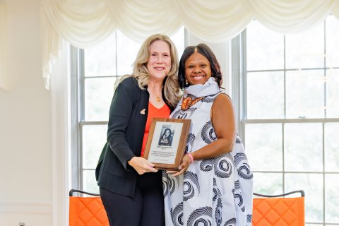 Two people hold a plaque while dressed in professional attire
