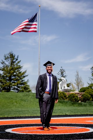 Photo of John in his graduation cap and down standing on the lacrosse field