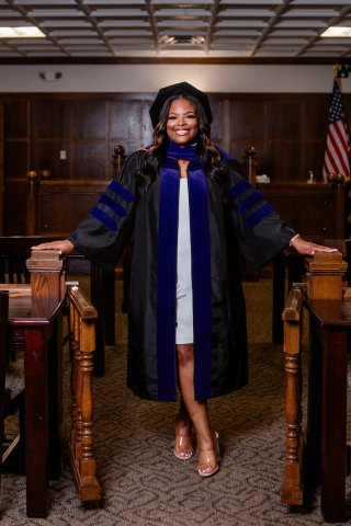 Photo of Aleeia in her graduation gown posing in the courtroom aisle