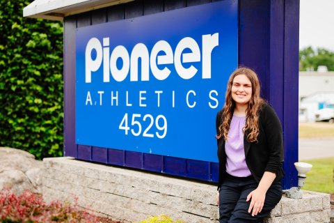 Photo of Ella standing next to a Pioneer Athletics Sign