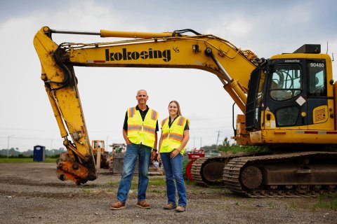 Photo of Isabelle posing with someone in front of a large excavator
