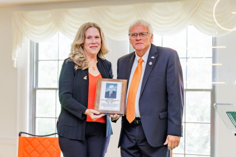 Two people hold a plaque while dressed in professional attire