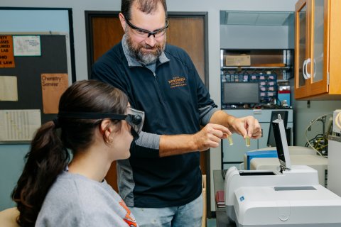 Close up photo of faculty helping ONU student with lab goggles on