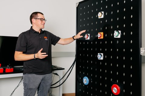 Photo of Josh pointing to a board with buttons on it