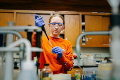Photo of Marissa in lab gear holding a vial in one hand