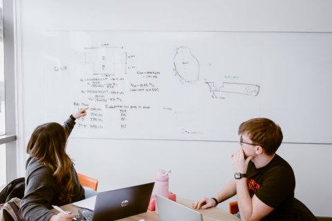 Another photo of the Engineering team pointing towards the whiteboard with notes on it