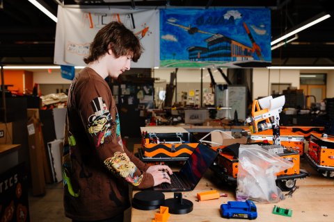Corbin on his laptop with his work project all around him on the table