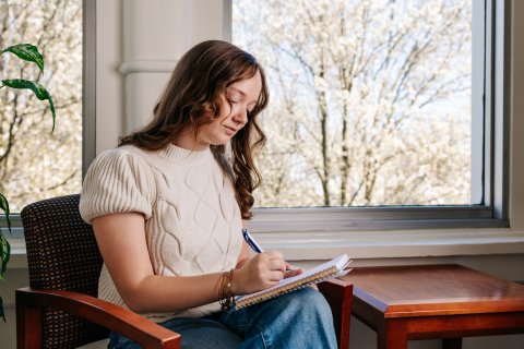 Evie seated on a chair writing in a notebook