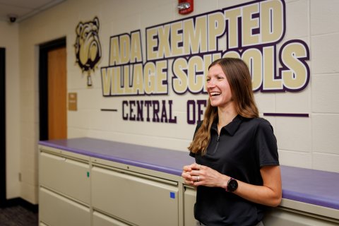 Tessa McVey smiling at with Ada Exempted Village Schools painted on the wall behind her