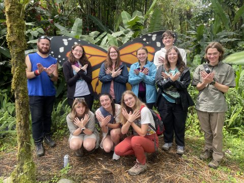 Photo of ONU students posing in front of a butterfly statue while creating butterflies with their hands