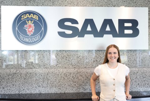 Photo of Rylie smiling next to a SAAB sign