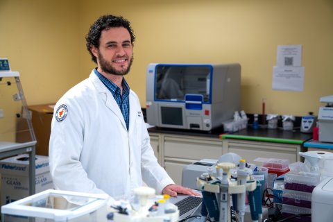 Photo of Klye in a white coat standing in front of a laptop