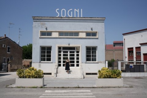 Photo of Jay posing in front of blue building with Sogni letters on top of it