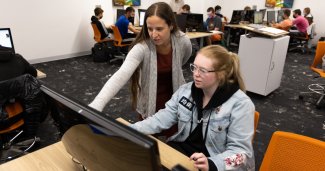 Photo of ONU student with the instructor over her shoulder working on the computer