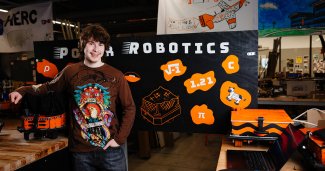 Corbin posing with a black robotics banner behind him and a laptop nearby