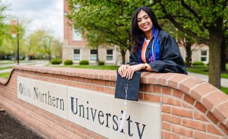 Simran in her cap and gown posing behind the brick outdoor sign that says ONU