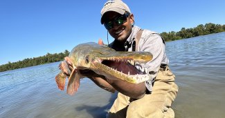 Dr. Solomon David, known as the 'Gar Guy,' holding a gar fish outdoors near the water.