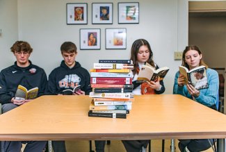 Four ONU students sitting at a table, each reading a book, with a stack of banned books in front of them.