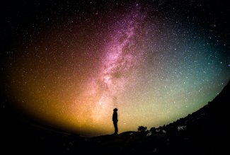 Person standing under starry sky, photo by Greg Rakozy on Unsplash.